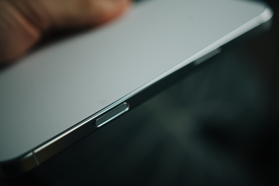 A detailed close-up of a smartphone, focusing on the smooth side profile and power button. The shallow depth of field emph...