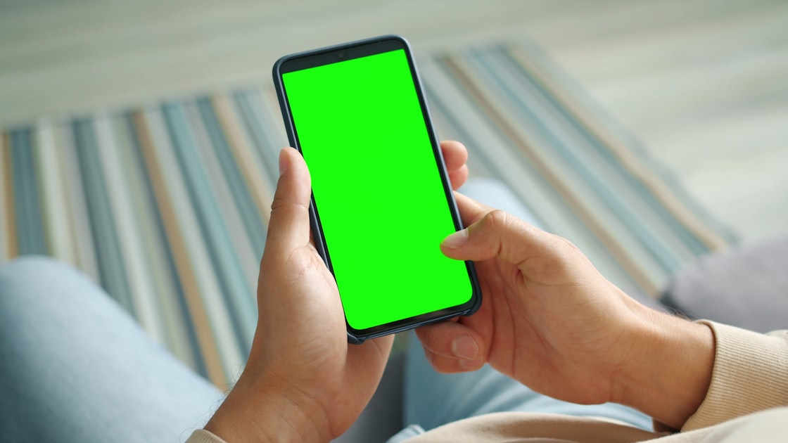 Male palms holding smartphone with mock-up green screen touching with fingers surfing internet enjoying online content. Pe...